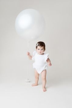 a baby girl is holding a white balloon