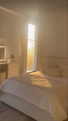 a bedroom with a bed, dresser and mirror in it's center area that has sunlight streaming through the window