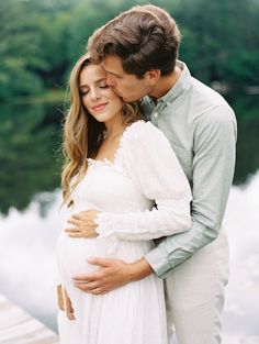 a pregnant couple cuddles in front of the water