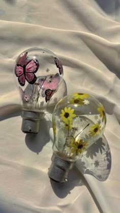 two light bulbs with butterflies on them sitting next to each other in the middle of a white sheet