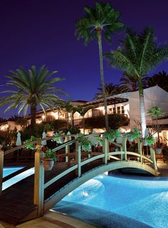 a bridge over a pool with palm trees in the background at night, near an apartment complex