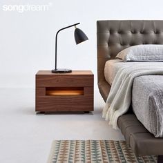 a bed sitting next to a night stand with a lamp on it's side