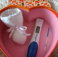 a pink heart shaped box with an electronic thermometer and baby booties in it