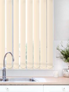 a kitchen with white cabinets and counter tops, window coverings in the shape of vertical blinds