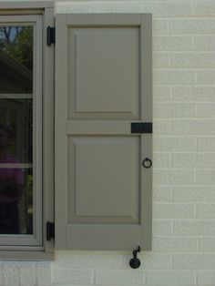 an open window on the side of a white brick building with grey shutters and black hardware