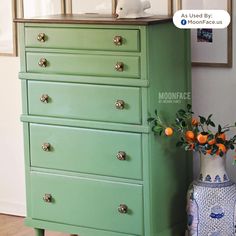 a green dresser with an orange vase on top