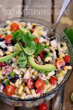 a glass bowl filled with pasta salad and garnished with cilantro, black olives, tomatoes, avocado