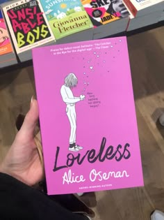 a person holding up a pink book in front of bookshelves with children's books on them