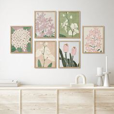 a white dresser sitting next to a wall with pictures on the wall and flowers hanging above it