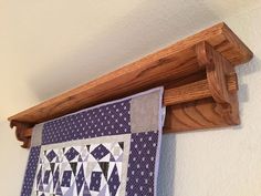 a quilt hanging on the wall next to a wooden coat rack with a purple and white patchwork design