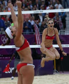 two women in bikinis are playing volleyball on the beach and one is jumping up to hit the ball