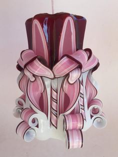 a pink and white candle holder hanging from a string on a wall in the shape of an ornament