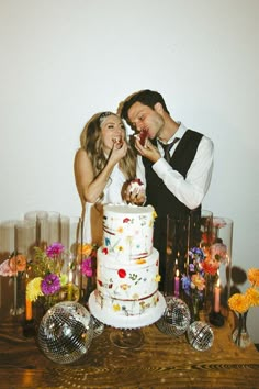 a man and woman standing in front of a cake on top of a wooden table