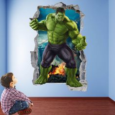 a boy sitting on the floor looking at an incredible hulk wall decal