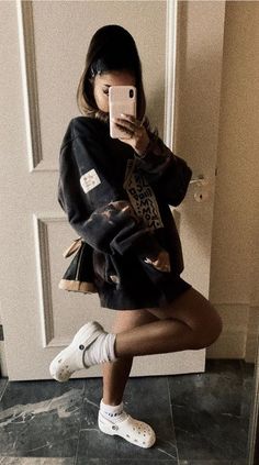 a woman taking a selfie in front of a door wearing white sneakers and a black jacket