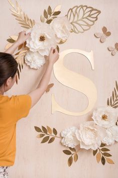 a woman is working on some paper flowers and the letters s are made out of gold foil