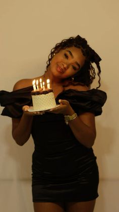 a woman holding a cake with lit candles on it in front of a white wall