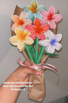 a hand holding a bouquet of paper flowers with a message written on the bottom right corner