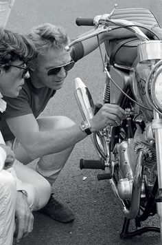 a man and woman sitting next to each other on the ground near a parked motorcycle