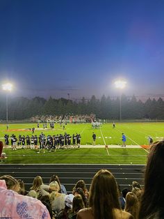 a football game is being played on a field at night with people sitting in the bleachers watching