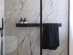 a bathroom with marble walls and flooring, black towel rack on the shelf next to the shower door