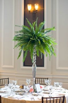 there is a tall plant in the center of this dining room set for two people