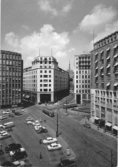 an old black and white photo of cars parked on the side of a road in front of tall buildings