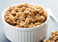 a white bowl filled with granola next to a spoon on top of a table