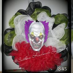 a creepy clown mask hanging on a wreath with red and green tulle around it