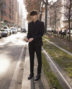 a man in a suit standing on the side of a road next to trees and buildings