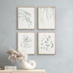 three framed pictures hang on the wall next to a dresser with a vase and plant