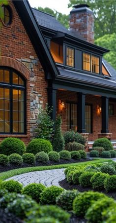 a brick house with lots of windows and bushes around the front yard, along with a circular stone walkway