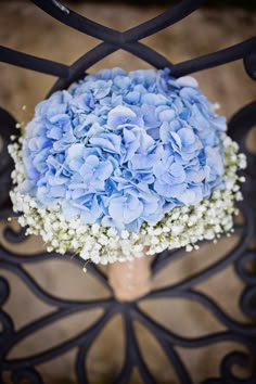 a bouquet of blue hydrangeas sitting on top of a wooden table next to a metal fence