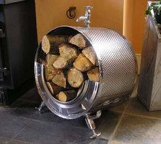 a bunch of wood that is inside of a metal barrel on the ground next to a fire place