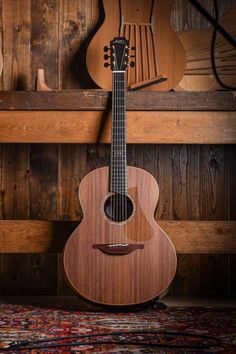 an acoustic guitar sitting on top of a rug in front of a wooden paneled wall