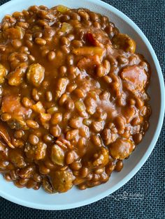 a white bowl filled with beans and meat on top of a blue table cloth next to a fork