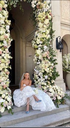 a woman in a wedding dress is sitting on the steps with flowers all around her