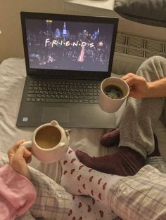 two children sitting on a bed with coffee in front of their laptops, one holding a cup and the other holding a mug