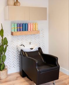 a black chair sitting in front of a sink under a shelf next to a potted plant