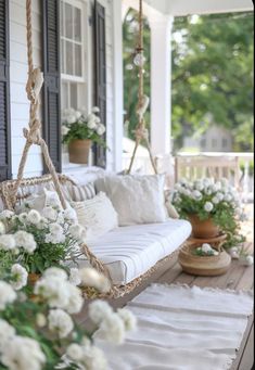 a porch swing with white flowers and greenery hanging from it's sides on the front porch