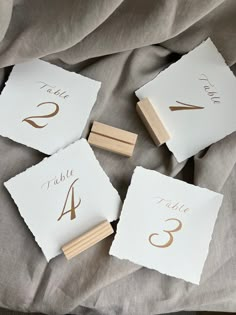 four wooden place cards with gold numbers on them sitting on a gray cloth covered bed