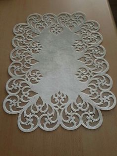 a white doily on a wooden table with an intricate design in the center and bottom