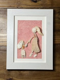 a white frame holds a pink paper cutout of a mother and child holding hands