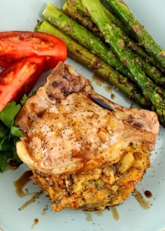 a white plate topped with meat and veggies next to asparagus on a table