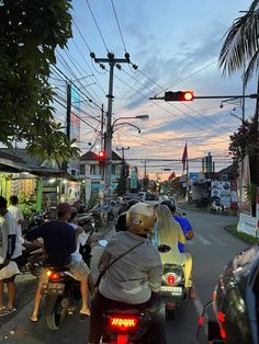 several people riding motorcycles down the street at dusk with traffic lights above them and palm trees in the background