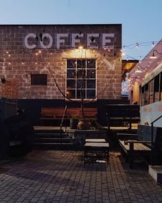 the outside of a coffee shop with lights strung from it's windows and benches