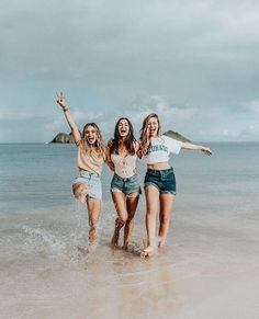 three young women are running in the water at the beach and one is holding her arms up