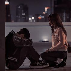 a young man sitting on the ground next to a woman