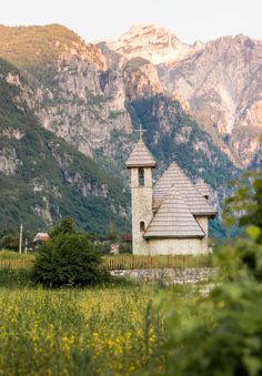 an old church in the middle of a field with mountains in the backgroud