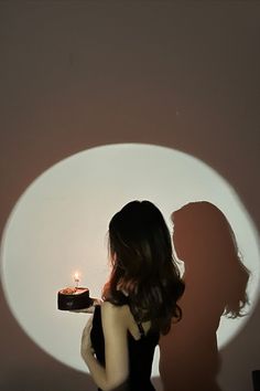 a woman holding a cake in front of a wall with the shadow of a man